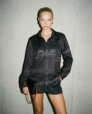 Model wearing a black outfit with text design against a gray concrete wall
