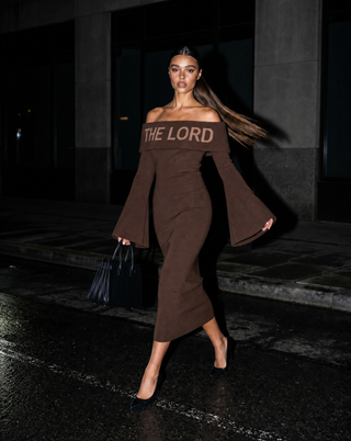 Woman wearing a brown off-shoulder top with 'THE LORD' text on a dark background