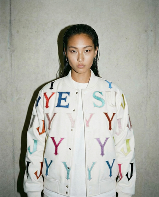 Person wearing a white jacket with colorful letters against a gray background