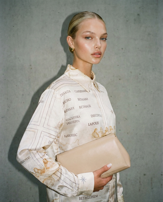 Woman holding a beige clutch against a gray background