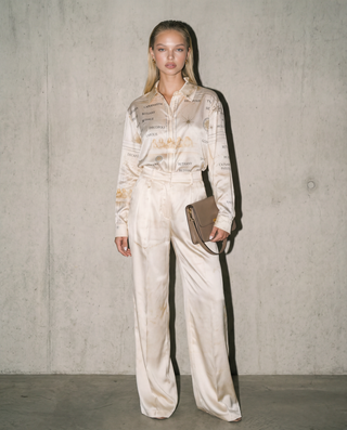 Woman wearing a cream-colored outfit with text design against a plain background