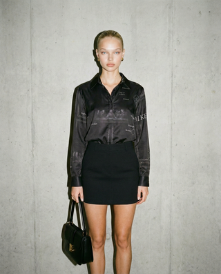 Woman wearing a black outfit with a logo against a gray concrete wall