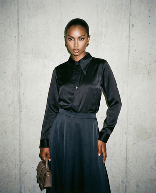 Woman wearing a black blouse and dark skirt against a gray concrete wall